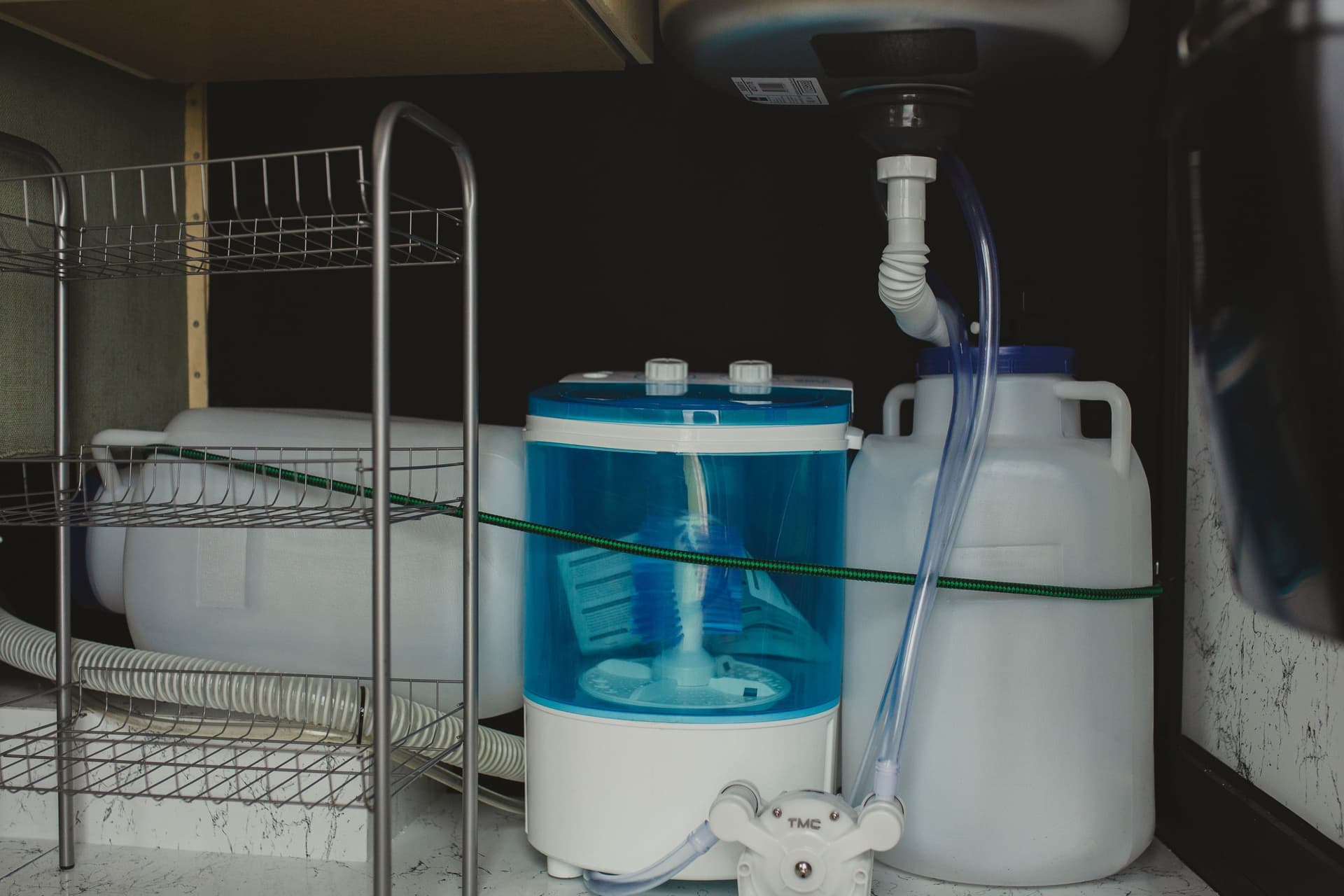 An open under-sink cabinet with cleaning bottles inside
