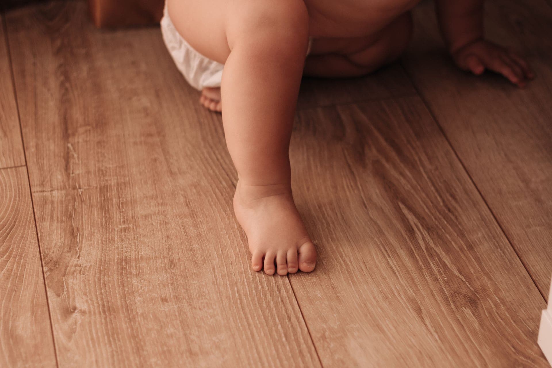 A baby crawling across a wooden floor toward a staircase