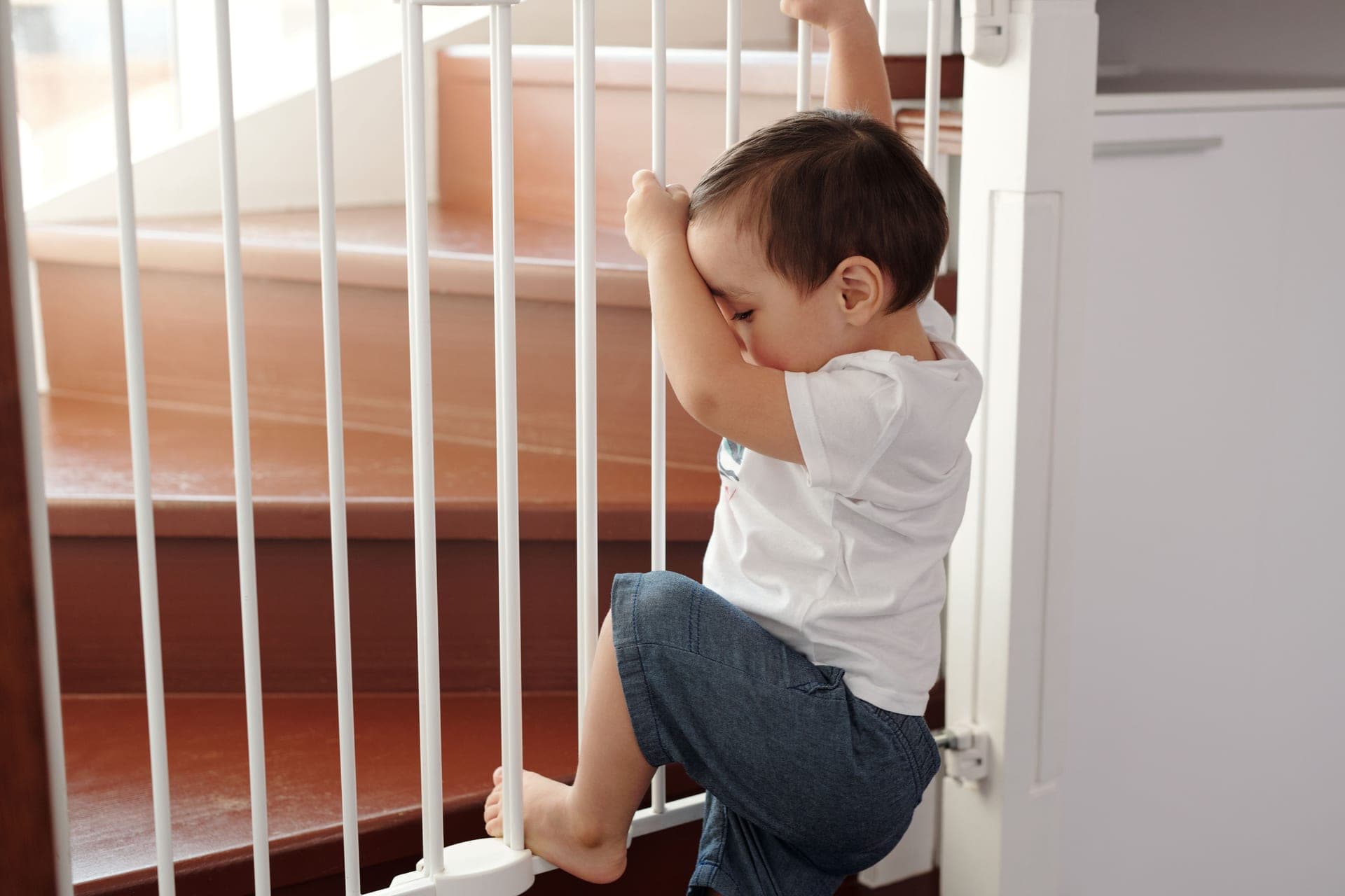 A white baby gate closed across the bottom of a wooden staircase