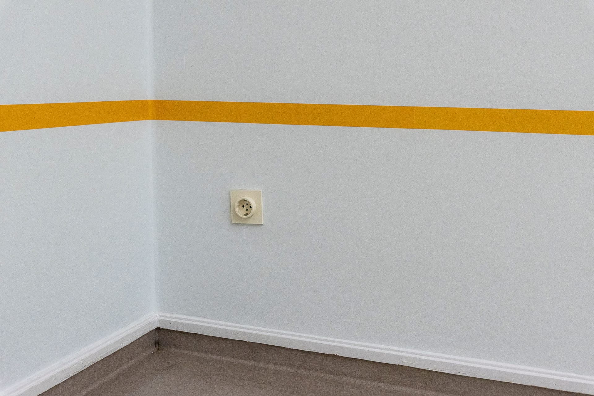 A white electrical outlet low on a wall beside a floor